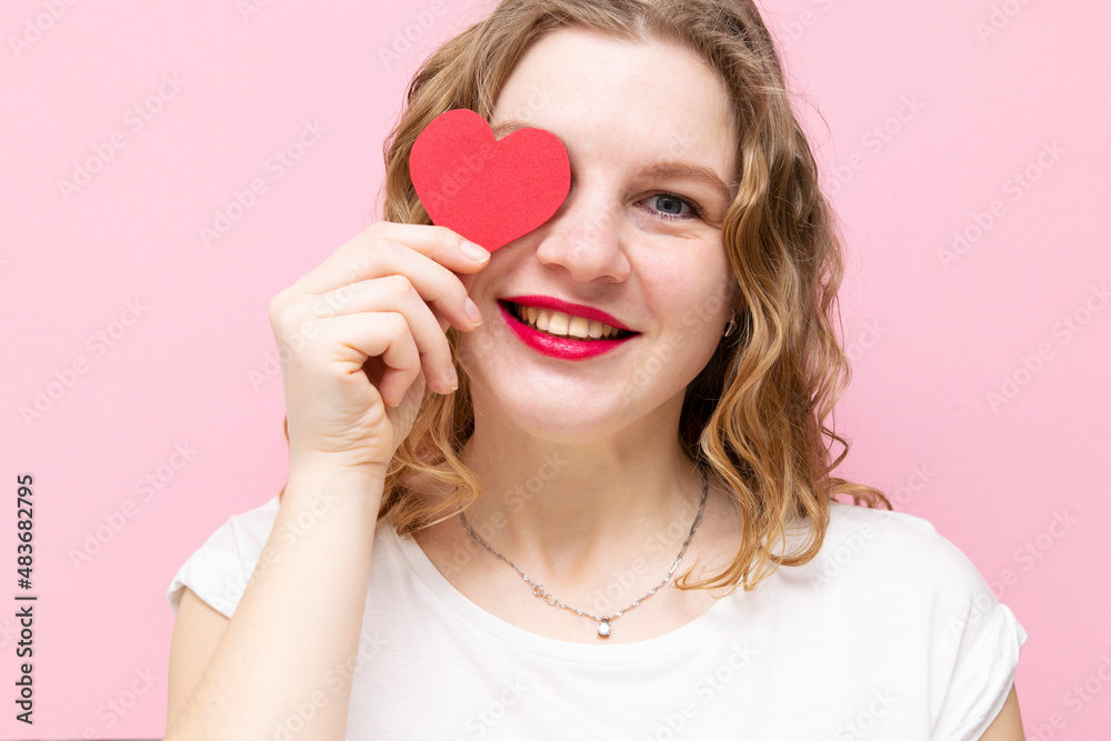 Attractive young woman smiling, having small red hearts in hands on pink background. Closing eyes with paper hearts Attractive young woman smiling, having small red hearts in hands on pink background. Closing eyes with paper hearts