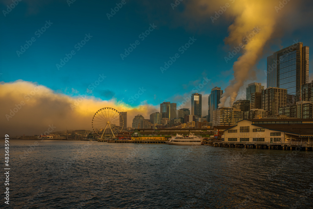 2022-01-29 THE SEATTTLE WATERFRONT WITH THE BIG WHEEL AND A CLOUD BANK MOVING IN AGAINST A BRIGHT BLUE SKY AND STEAM RIDING FROM A DOWNTOWN BUILDING