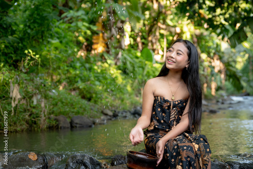 Beautiful young Asian girl rests in the river and making water drops