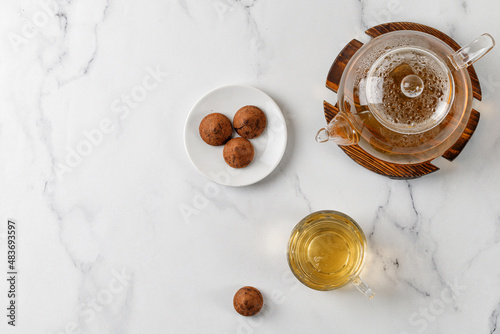 Glass with green herbal tea  with sweets truffles and teapot on white marble background. Top view. Copy space