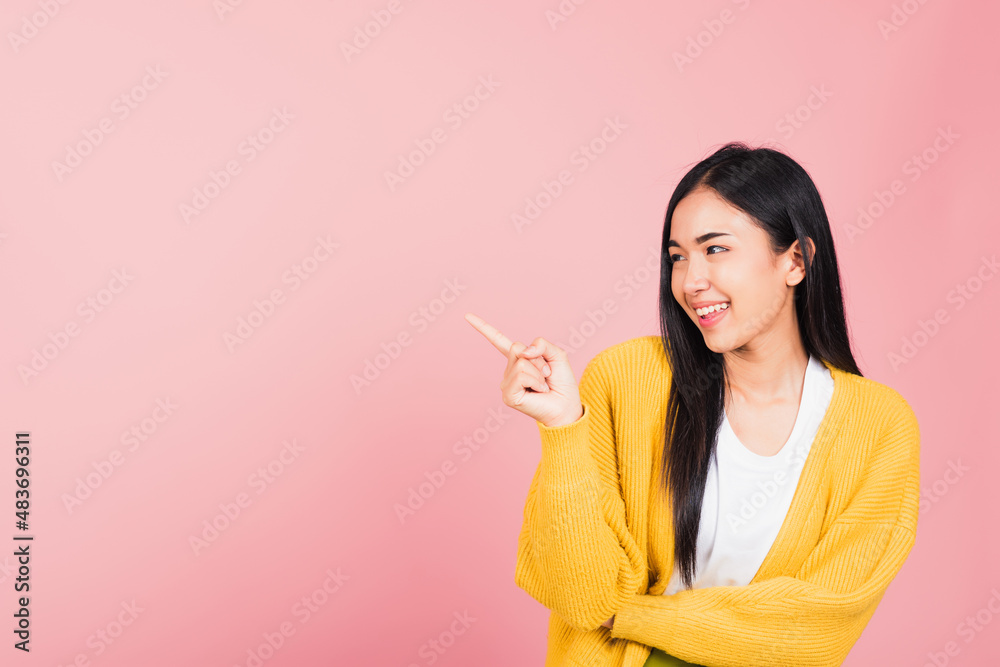 Asian happy portrait beautiful cute young woman standing pointing finger side away presenting product looking to away side, studio shot isolated on pink background with copy space Asian happy portrait beautiful cute young woman standing pointing finger side away presenting product looking to away side, studio shot isolated on pink background with copy space