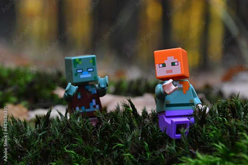 Naklejka premium LEGO Minecraft figure of Alex chased by hostile Drowned Zombie mob on moss surface in real autumn forest