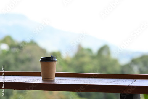 Take away cup of coffee placed on the wooden balcony edge with natural background.