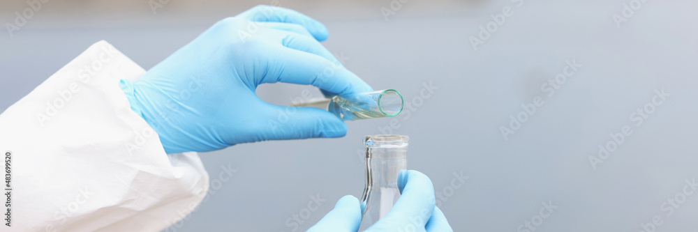 Scientist in gloves and protective suit pours dirty water from test tube into flask Scientist in gloves and protective suit pours dirty water from test tube into flask
