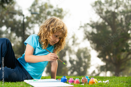 Children creative, developing imagination, creativity. Child boy enjoying art and craft drawing in backyard or spring park. Children drawing draw with pencils outdoor.
