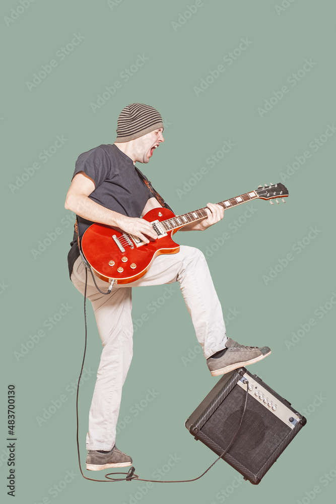 Rockstar with guitar leans foot on amp while playing. Full length vertical shot of vocalist playing guitar and screaming and growling his voice. Rock musician is playing electrical guitar