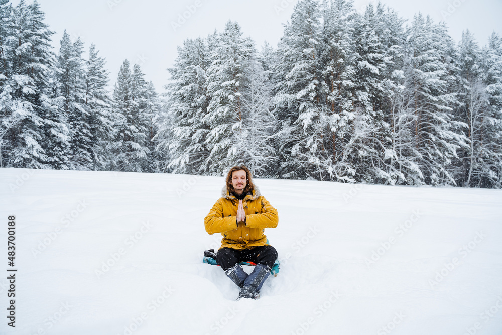 A happy man rejoices in the snowfall. A man sits in the snow.Meditation. Panoramic view of the forest. A walk in the forest in winter