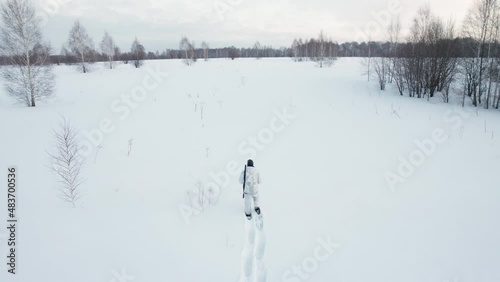A hunter in winter camouflage and snowshoes walks through a winter forest.