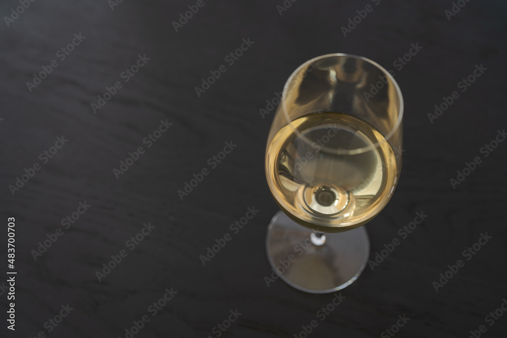 White wine in a wineglass on black oak table with copy space