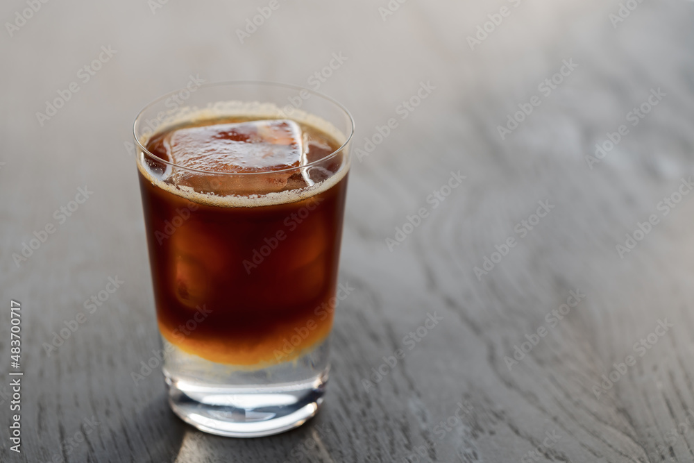 Espresso tonic with clear ice cube in tumbler glass on oak wood table with copy space