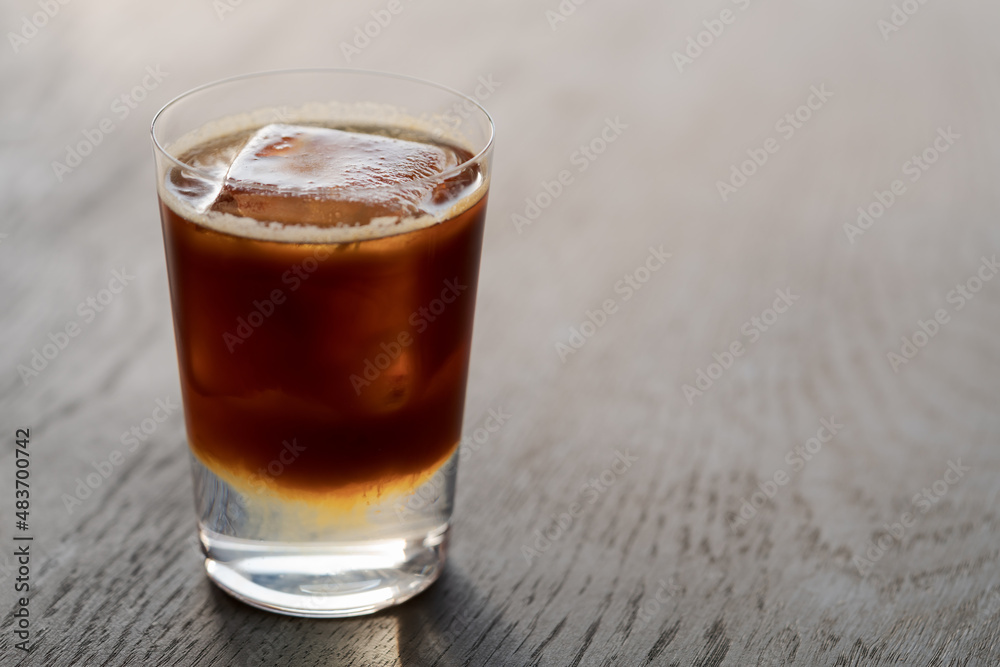 Espresso tonic with clear ice cube in tumbler glass on oak wood table with copy space Espresso tonic with clear ice cube in tumbler glass on oak wood table with copy space
