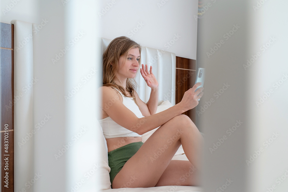 Woman sitting on the bed in hotel room texting on mobile phone