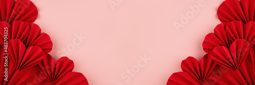 Valentines day banner - beautiful red paper ribbed hearts in simple origami style on pastel pink color as sideways border, frame, copy space, top view.