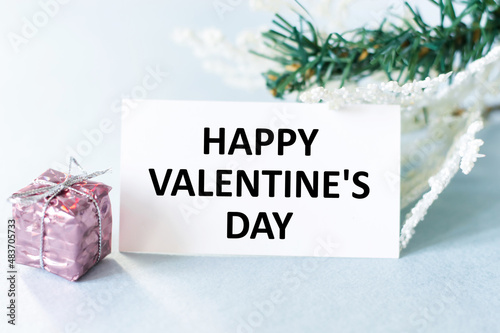 Happy Valentine's Day text on the card next to a gift in pink packaging and spruce two branches, a feast of lovers, love