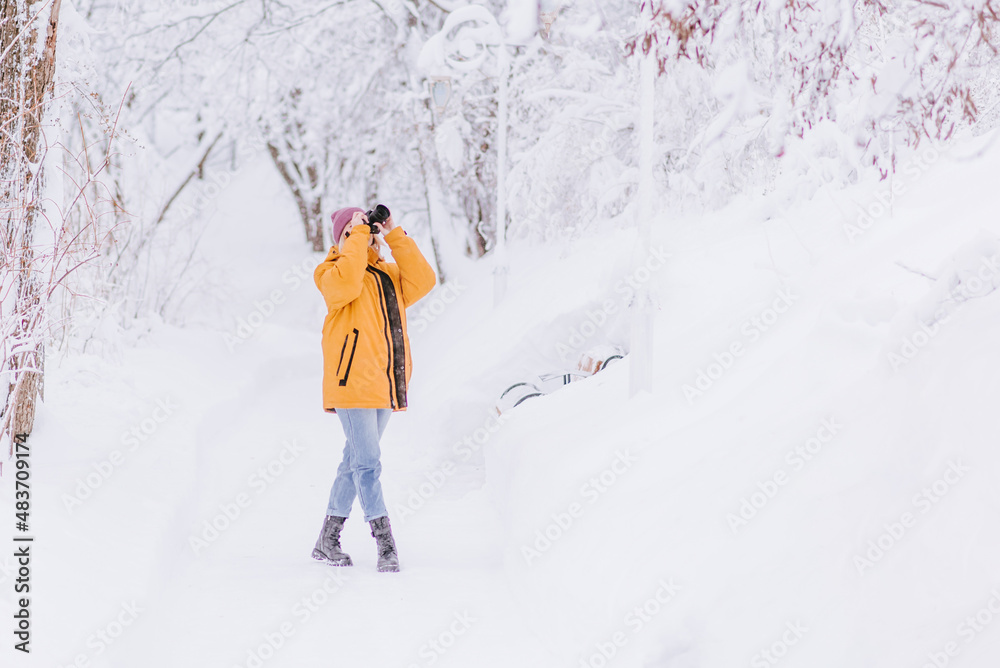 Beautiful girl in a yellow jacket photographer takes pictures of snow in a winter park