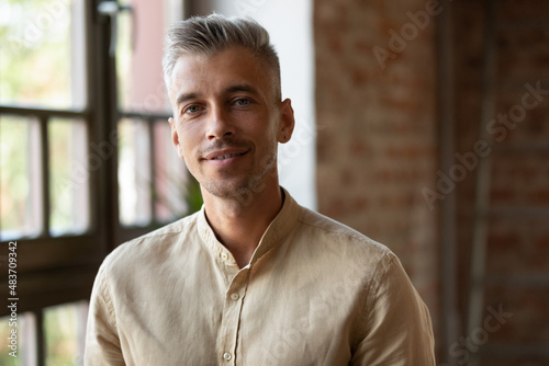 Happy positive millennial business man in casual, company owner, startup leader, professional posing, looking at camera, smiling. Businessman indoor head shot portrait in loft interior