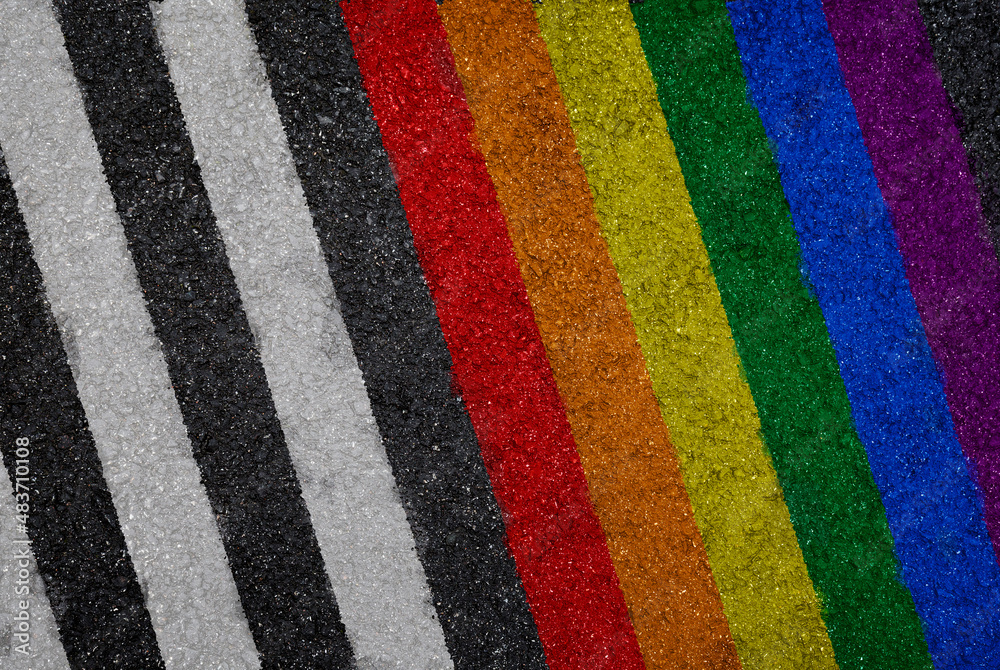 Rainbow colored LGBT pride flag painted next to white lines on asphalt, top view. High resolution full frame textured background of colorful striped asphalt, viewed from above. Copy space.