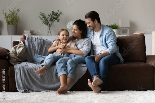 Loving parents and daughter sit on sofa enjoy time together communicating sit on sofa in cozy living room. Offspring upbringing and custody, understanding, good harmonic relations, family bond concept