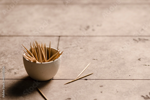 A small bowl of toothpicks on the edge of a table with a few scattered on the table. photo