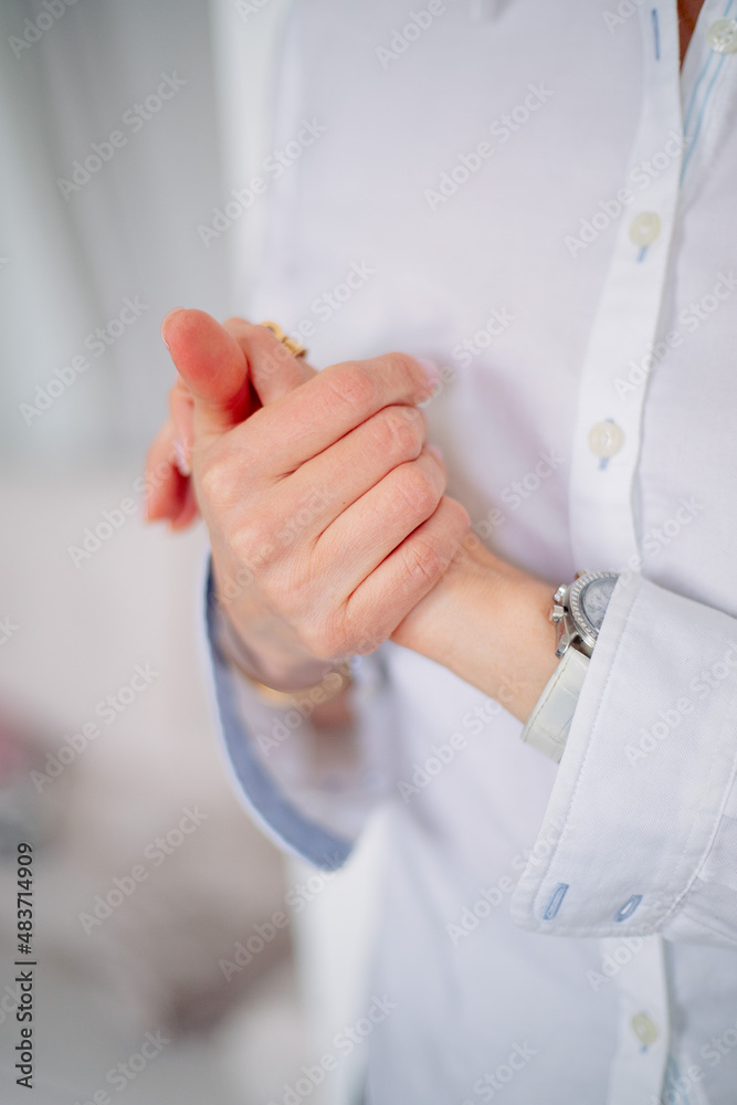 A girl in a buttoned white shirt with unbuttoned cuffs of her sleeves closed her hands.