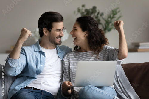 Tableau sur toile Couple sit on sofa with laptop clenched fists make yes gesture celebrate great news