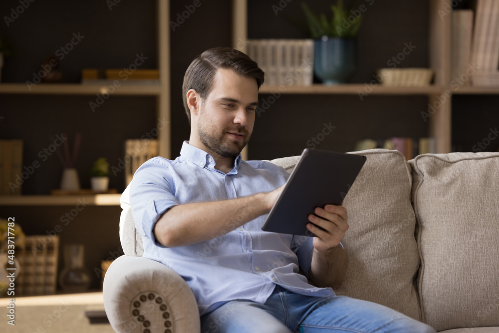 Relaxed smiling young man using digital touchpad gadget, enjoying web surfing information, playing entertaining online game, texting message communicating in social network, modern tech addiction. Relaxed smiling young man using digital touchpad gadget, enjoying web surfing information, playing entertaining online game, texting message communicating in social network, modern tech addiction.