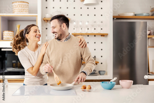 A happy couple making eggs for breakfast in the kitchen at their cozy apartment.