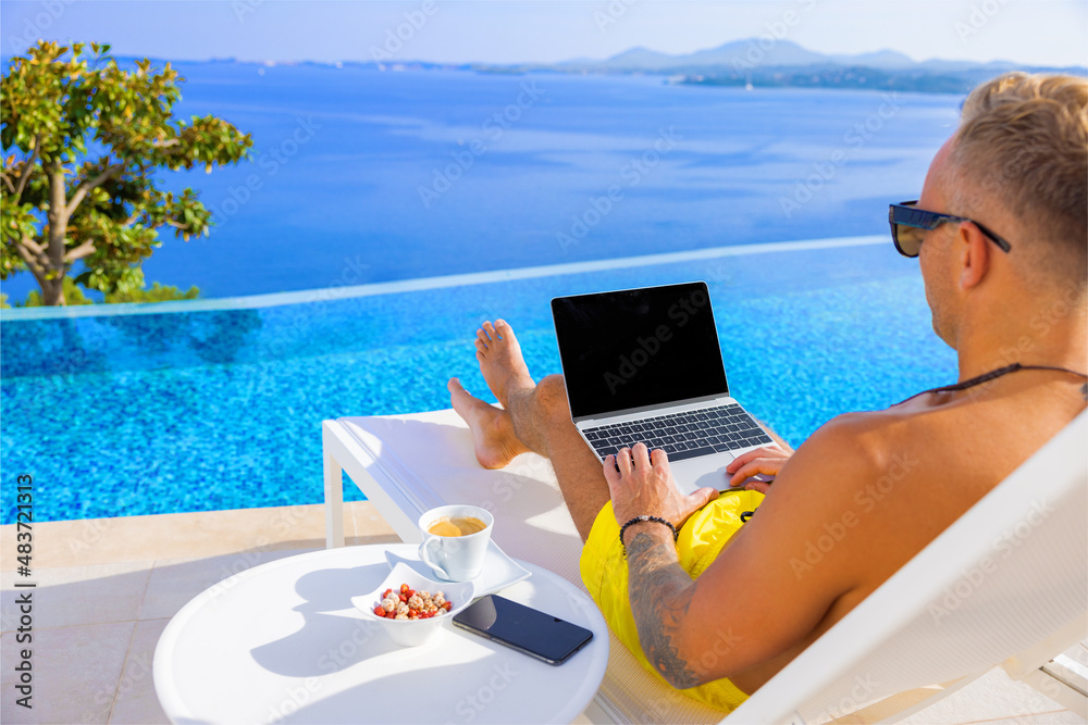 Man working on laptop computer outdoors by the pool