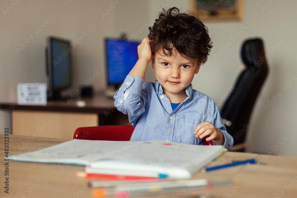 Preschool education online. A cheerful and energetic preschooler at the computer is engaged, next to notebooks, pencils. Lesson with a teacher remotely. Preschool education online. A cheerful and energetic preschooler at the computer is engaged, next to notebooks, pencils. Lesson with a teacher remotely.