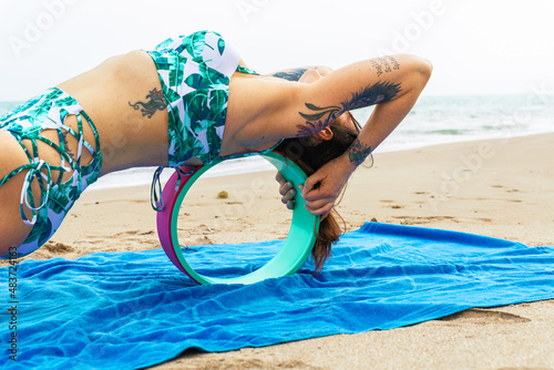 Butera, Italy – 26.06.2021: Side view of a mature person practicing pigeon yoga pose with a help of yoga wheel - doing purvottanasana yoga pose with wheel - Mature person doing yoga on a cork wheel in photo