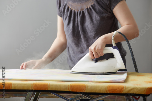 female hands are holding a white iron and iron on an ironing board. Close-up. Faceless. Copy space on gray background. Household duties and home care