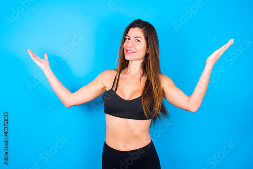 Cheerful Young beautiful sportswoman doing sport wearing sportswear over blue background making a welcome gesture raising arms over head.