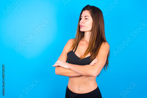 Image of upset Young beautiful sportswoman doing sport wearing sportswear over blue background with arms crossed. Looking with disappointed expression aside after listening to bad news.
