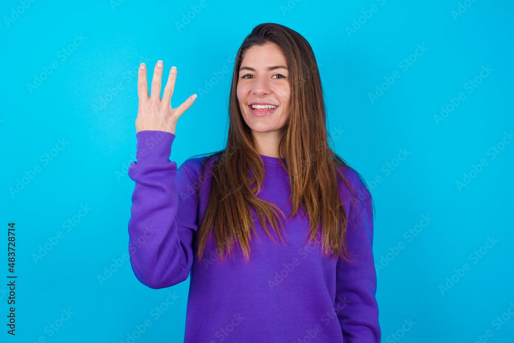Fototapeta premium young beautiful caucasian woman wearing purple sweater against blue background smiling and looking friendly, showing number four or fourth with hand forward, counting down