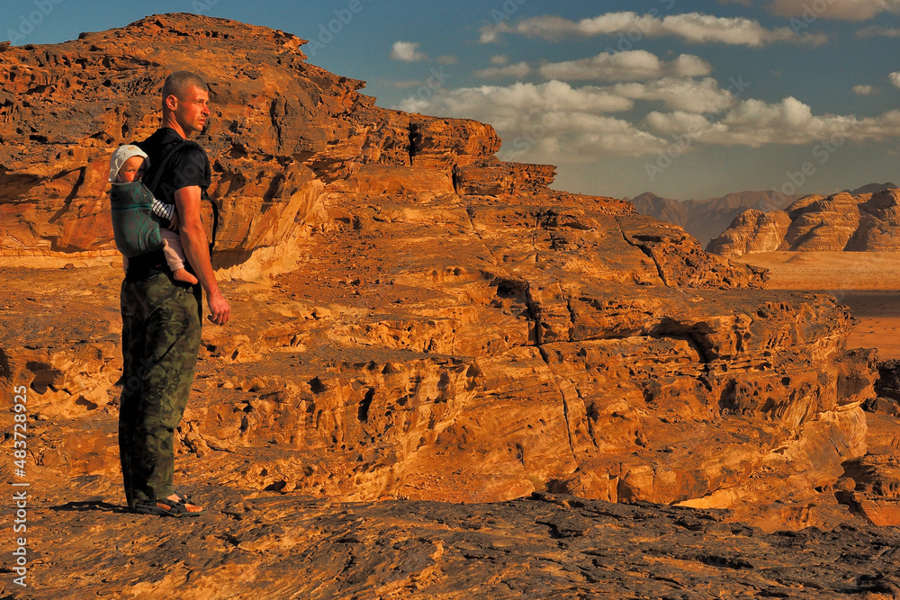 A father with a infant daughter in a baby carrier sightseeing the mountains. Wadi Rum, Jordan.