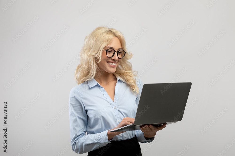 Online business. Happy businesswoman using laptop computer for online work or studies over light grey studio background Online business. Happy businesswoman using laptop computer for online work or studies over light grey studio background