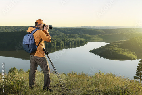 Mature traveller man with backpack standing in mountain and taking a photo. Happy man hiking with backpack at sunset.