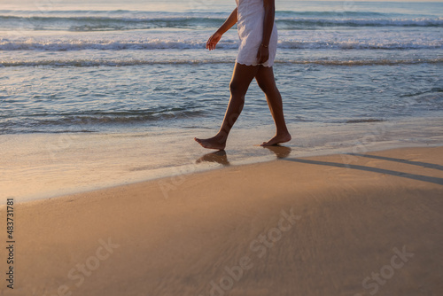 Cropped view of the legs of an anonymous woman walking along the beach at sunset