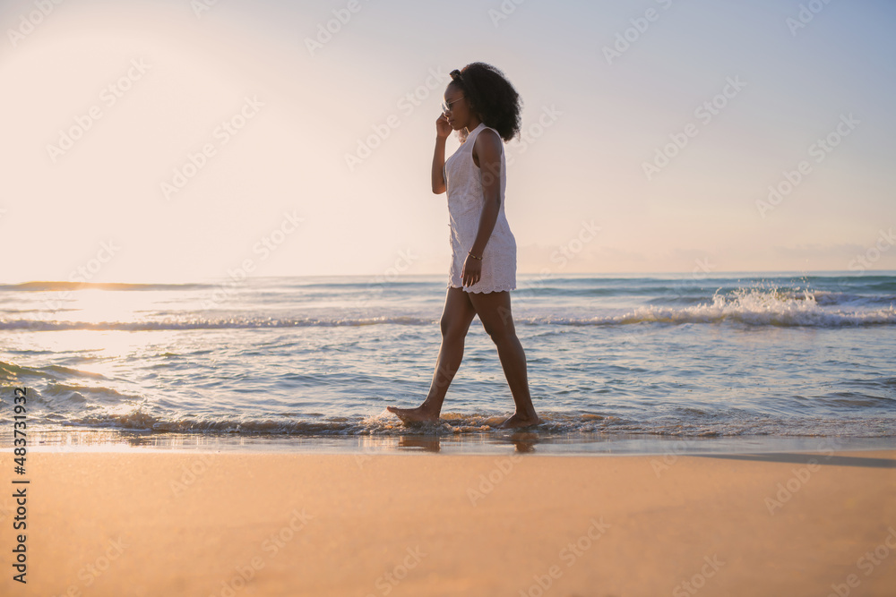 African american woman walking along the beach at sunset