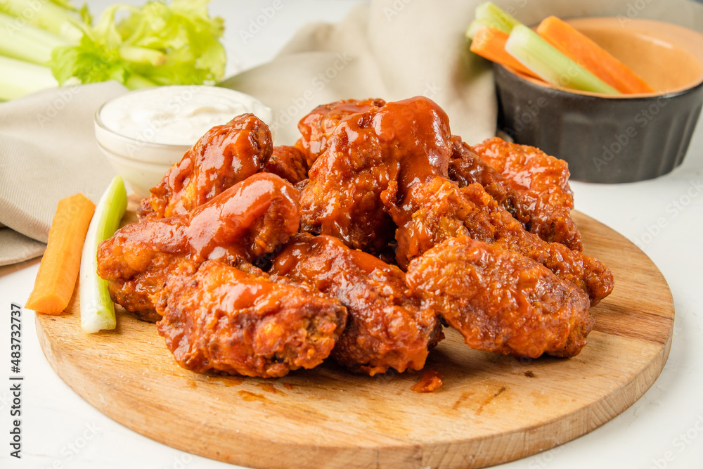 Fried bbq wings a lot, served on a wooden board with celery and carrot vegetables and blue cheese sauce. Traditional buffalo wings.