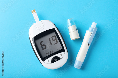 Digital glucometer and lancet pen on light blue background, flat lay. Diabetes control photo