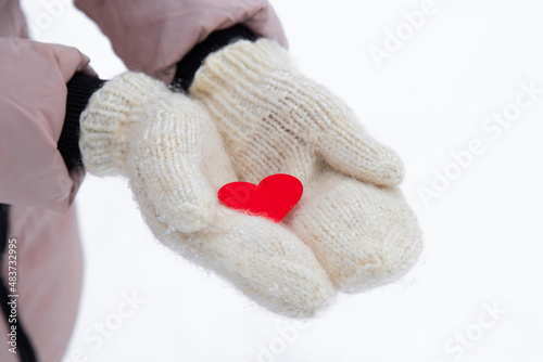 red heart lies on the fresh mittens. Winter snow. the woman dares in her palms a small red heart. close-up.