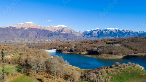 Aerial view of Scandello lake in Amatrice, Italy. Beautiful autumn landscape with lake, forest and mountains with snow-capped peaks in the background.