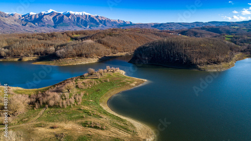 Aerial view of Scandello lake in Amatrice, Italy. Beautiful autumn landscape with lake, forest and mountains with snow-capped peaks in the background.
