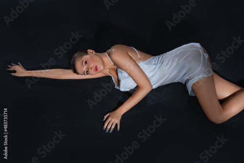 Attractive young woman under water drops isolated on black background.Sexy beautiful woman posing in white dress under water.Fashion style portrait