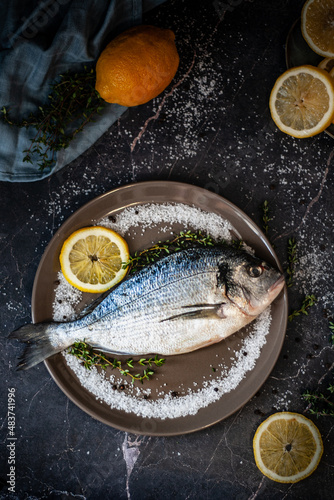 Fresh fish dorado with lemon, thyme and sea salt on a clay plate on a marble table