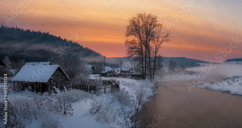 old village near the river against the backdrop of the mountains on a winter evening at sunset © Lana Kray
