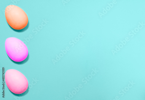 Three Easter eggs colored with violet, pink and coral colors from left side on a blue background. Flat lay. Copy space for text, mock up. Banner.