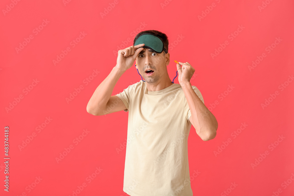 Shocked young man with sleeping mask and ear plugs on red background Shocked young man with sleeping mask and ear plugs on red background