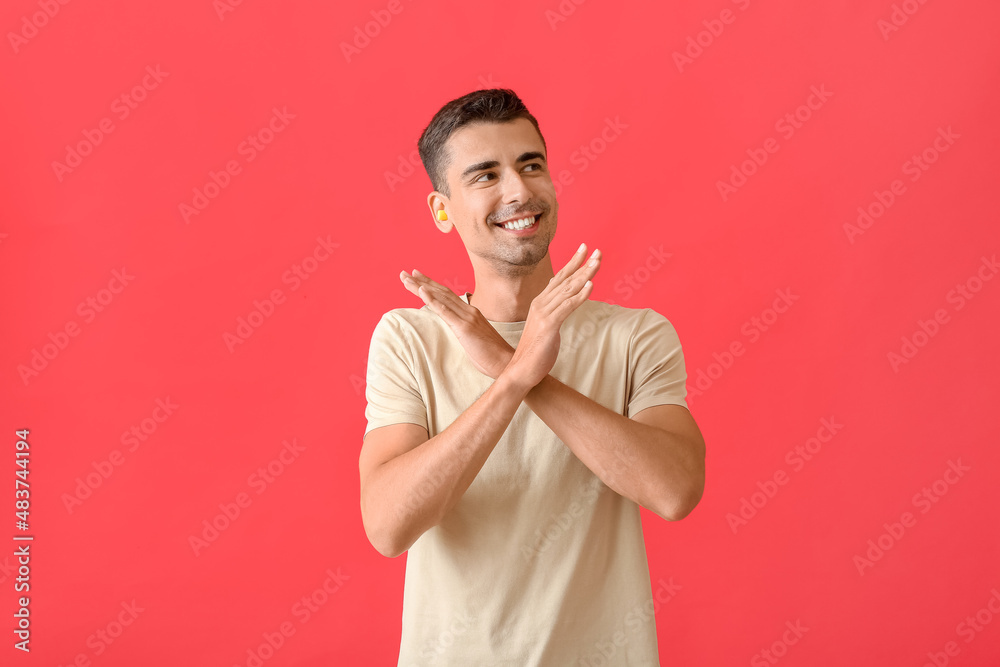 Smiling young man with ear plugs showing stop gesture on red background Smiling young man with ear plugs showing stop gesture on red background